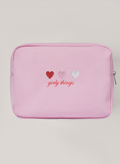Pink waffle pouch with 'girly things' text and heart designs on a light grey background