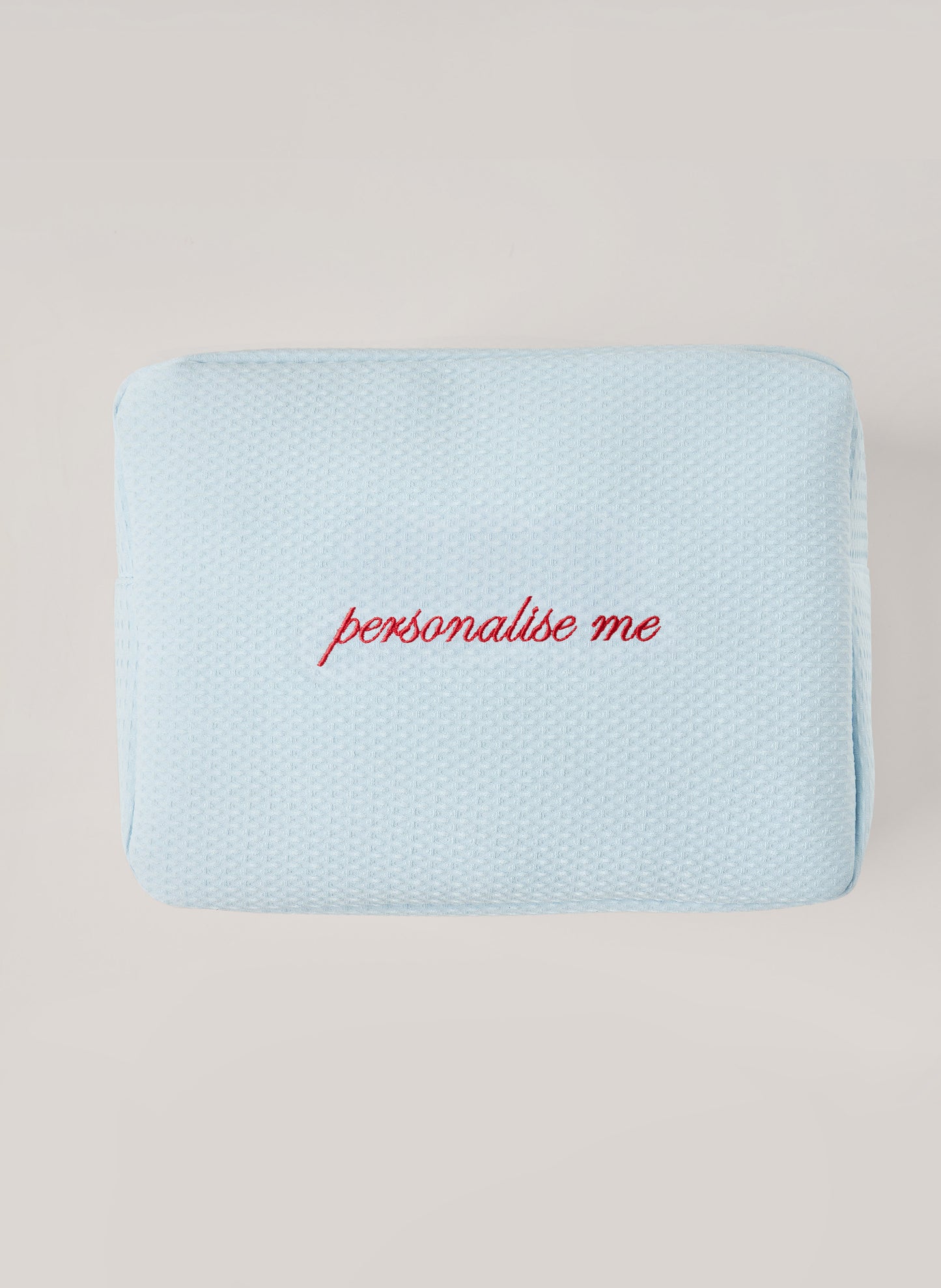 Light light blue waffle-textured pouch with zipper closure, featuring a red embroidered heart and the words 'personalise me’ on the front