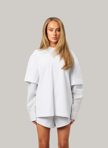Woman wearing a light gray oversized sweater on a plain background