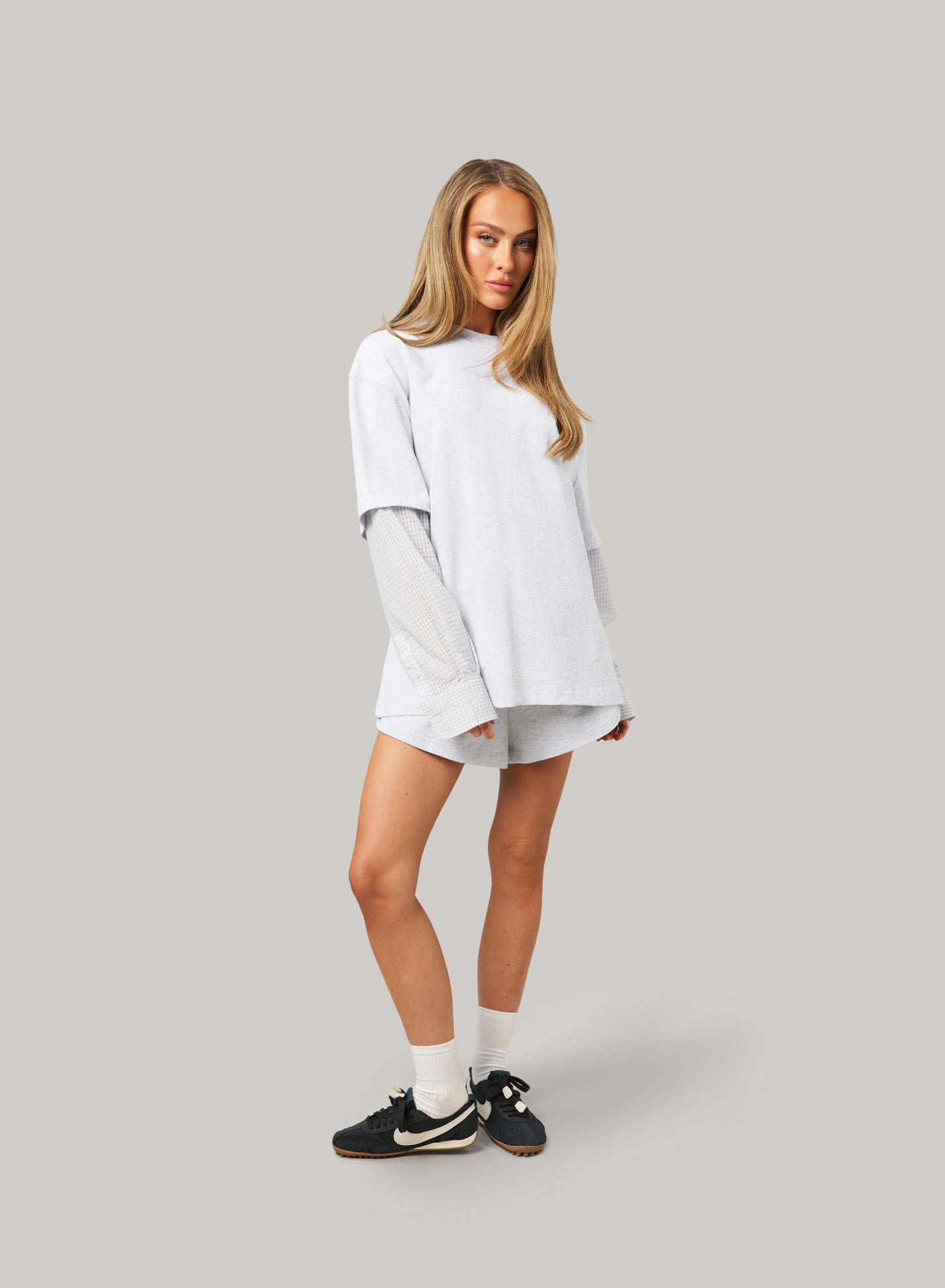 Woman wearing a light gray oversized sweater and shorts on a plain background