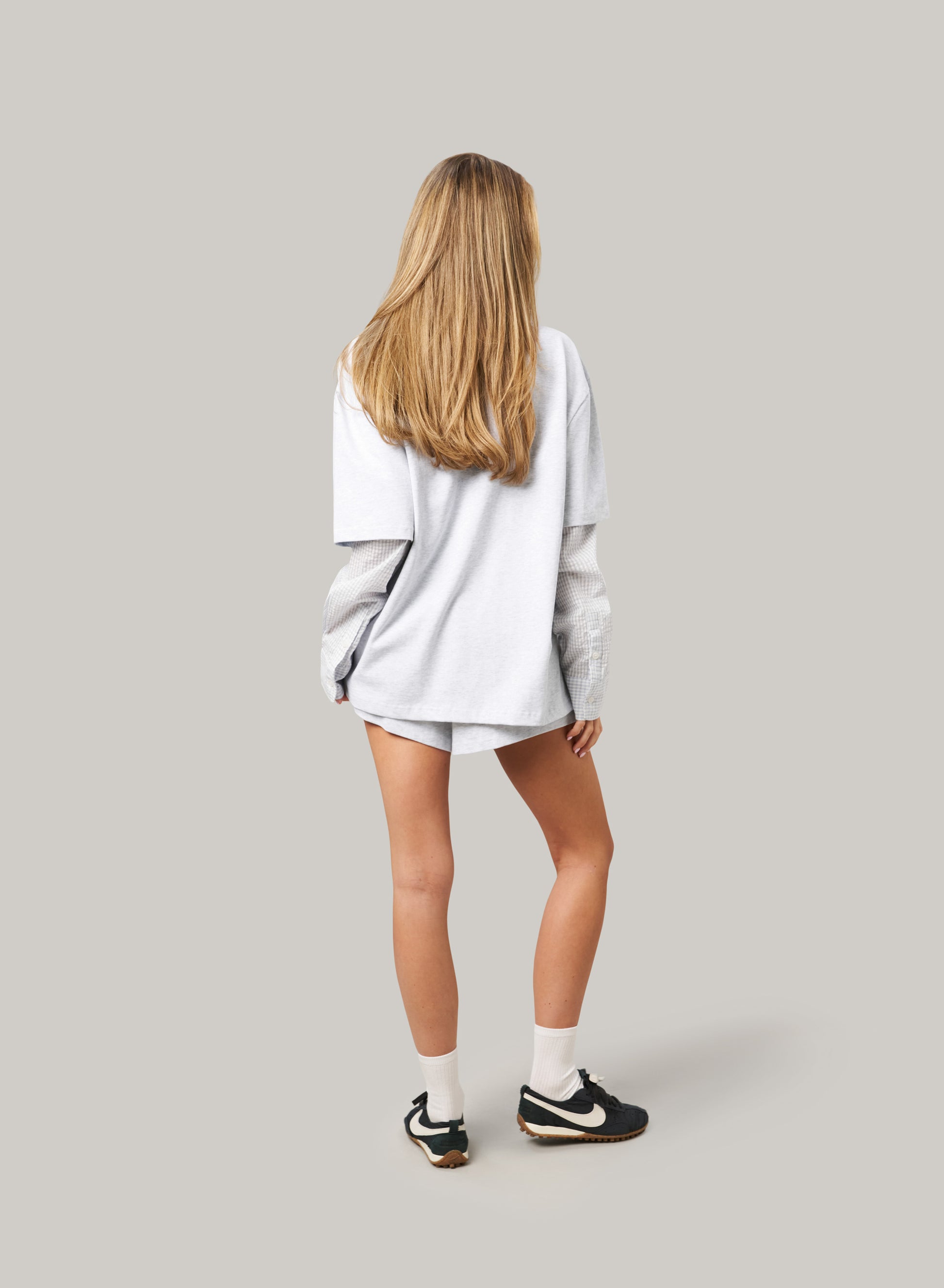 Person wearing a light gray oversized sweatshirt and shorts on a plain background