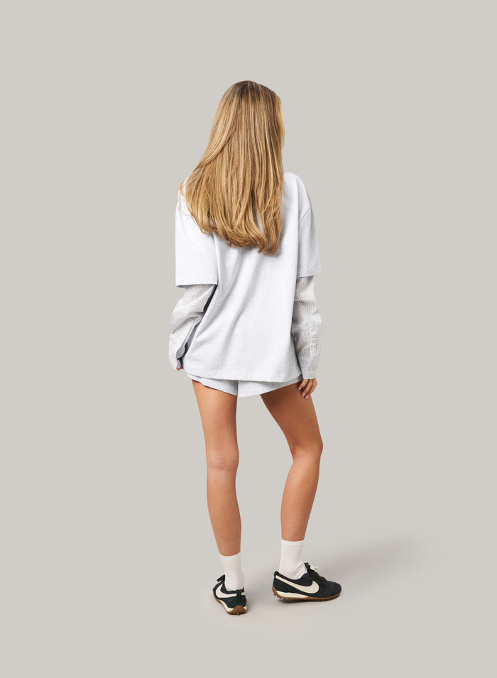Person wearing a light gray oversized sweatshirt and shorts on a plain background