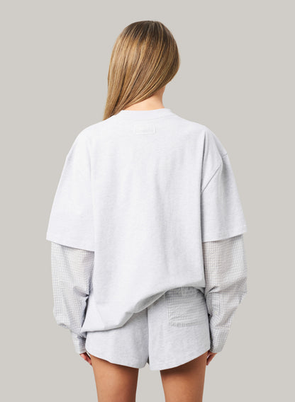 Person wearing a light gray oversized shirt and shorts set on a plain background