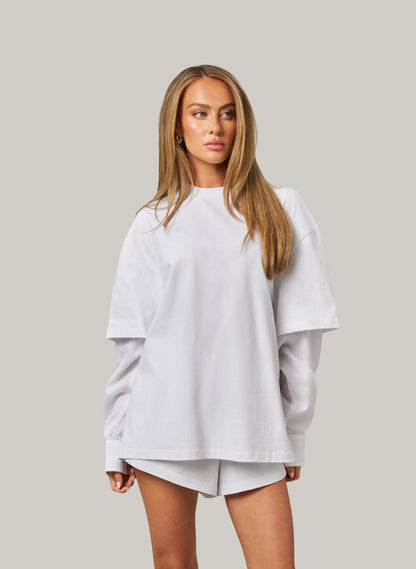 Woman wearing a white oversized sweatshirt and shorts on a plain background