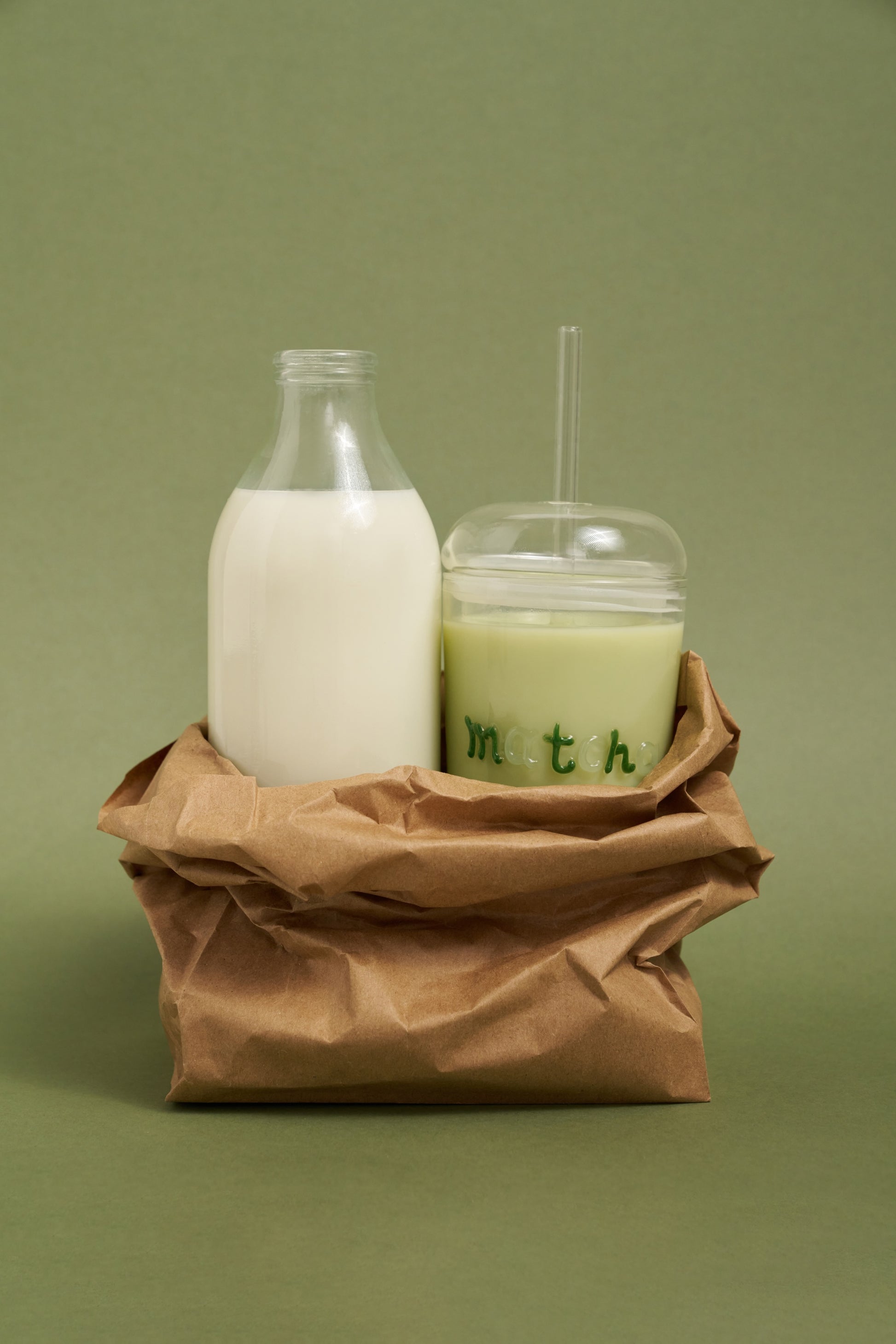 Milk bottle and glass with straw on a brown paper bag against a green background