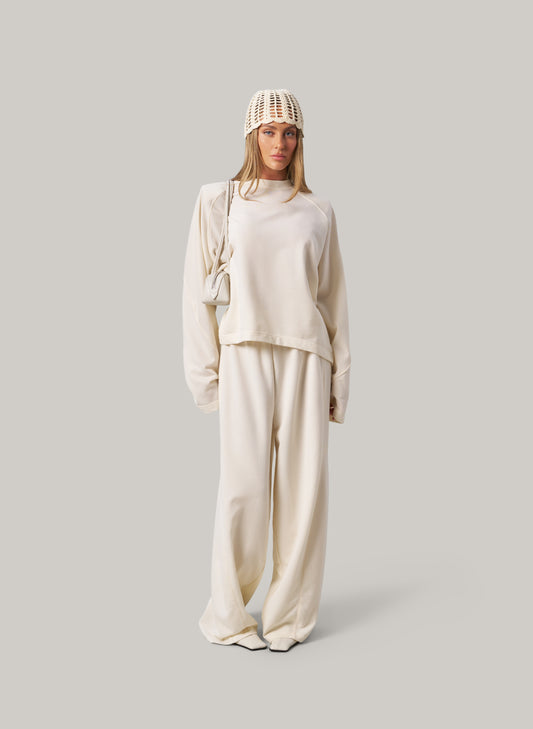 Person wearing a beige outfit with a knit hat on a light gray background