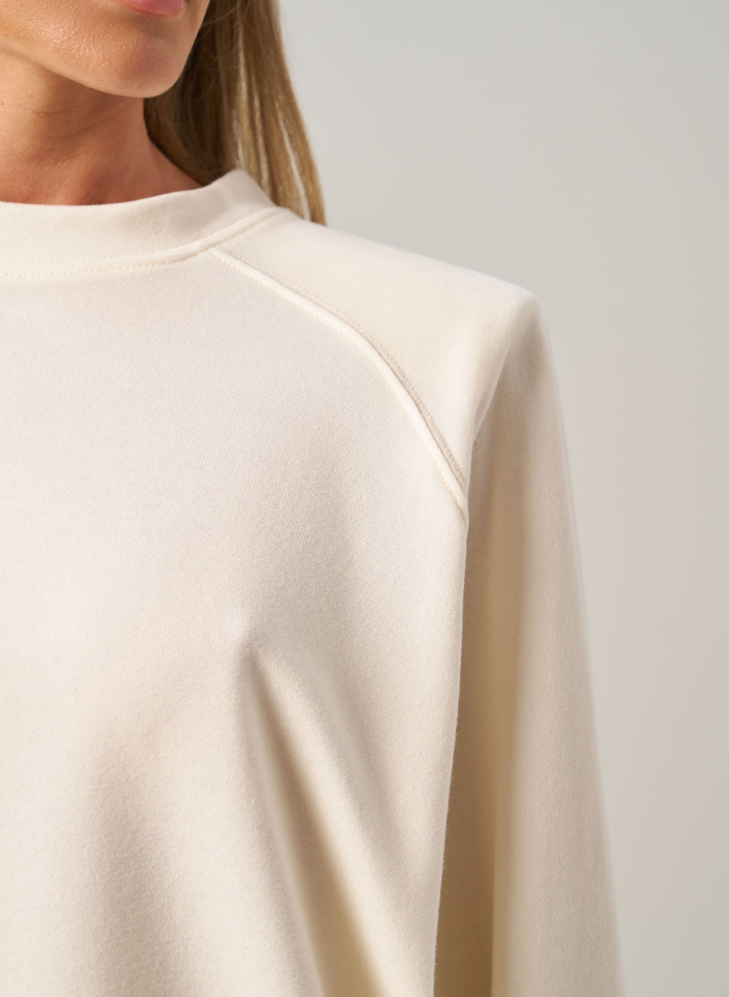 Close-up of a person wearing a beige long-sleeve top against a neutral background
