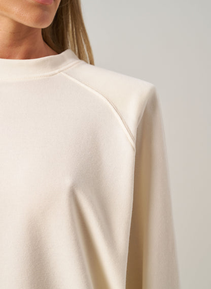Close-up of a person wearing a beige long-sleeve top against a neutral background