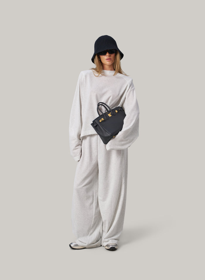Person wearing a white outfit with a black hat and bag on a light grey background