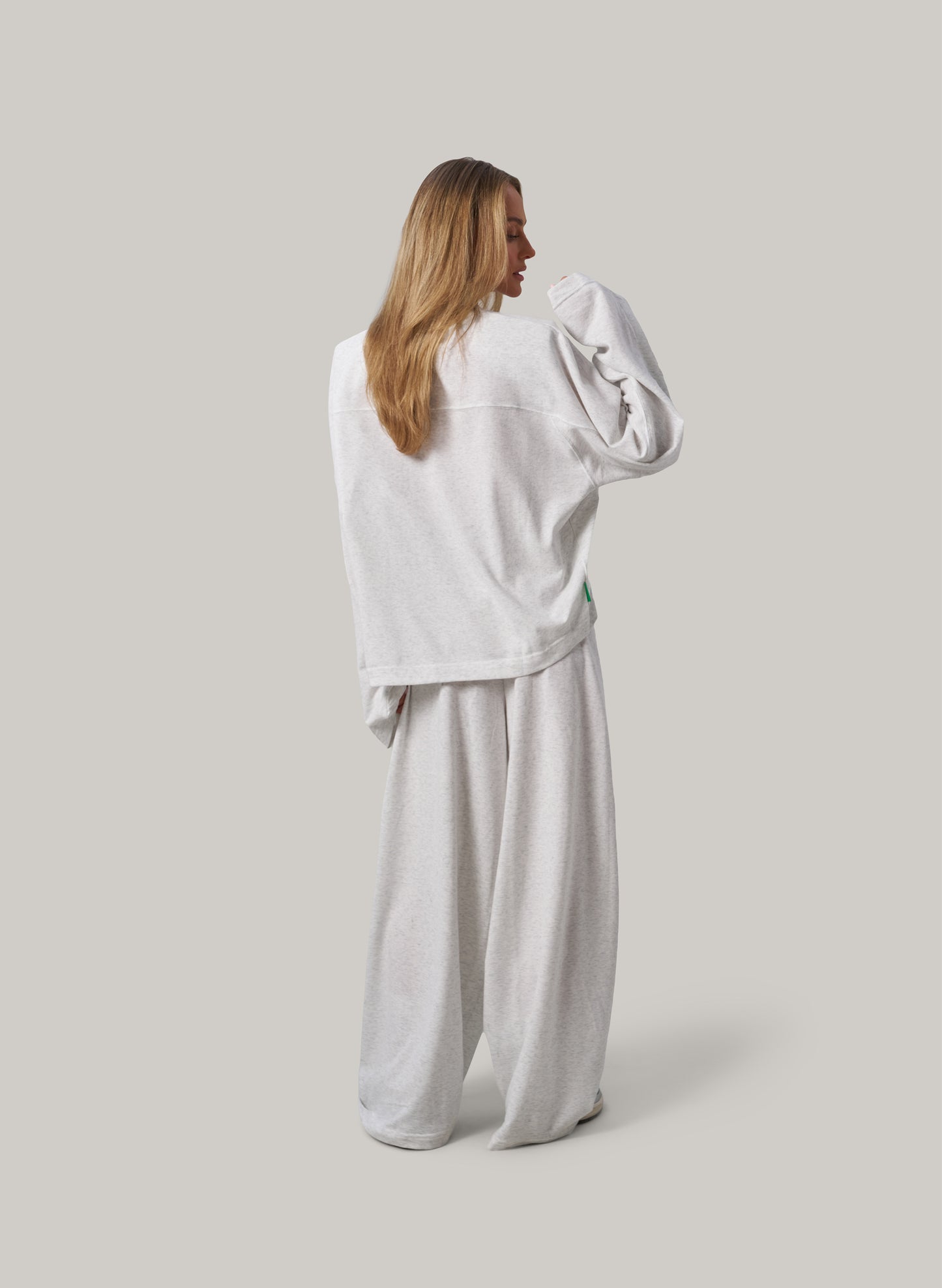 Woman wearing a light grey sweatshirt and pants on a plain background