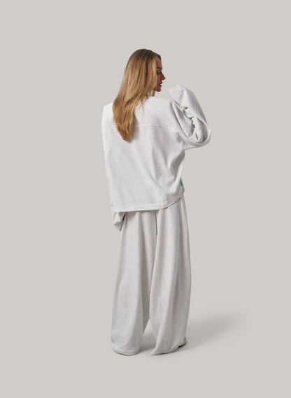Woman wearing a light grey sweatshirt and pants on a plain background