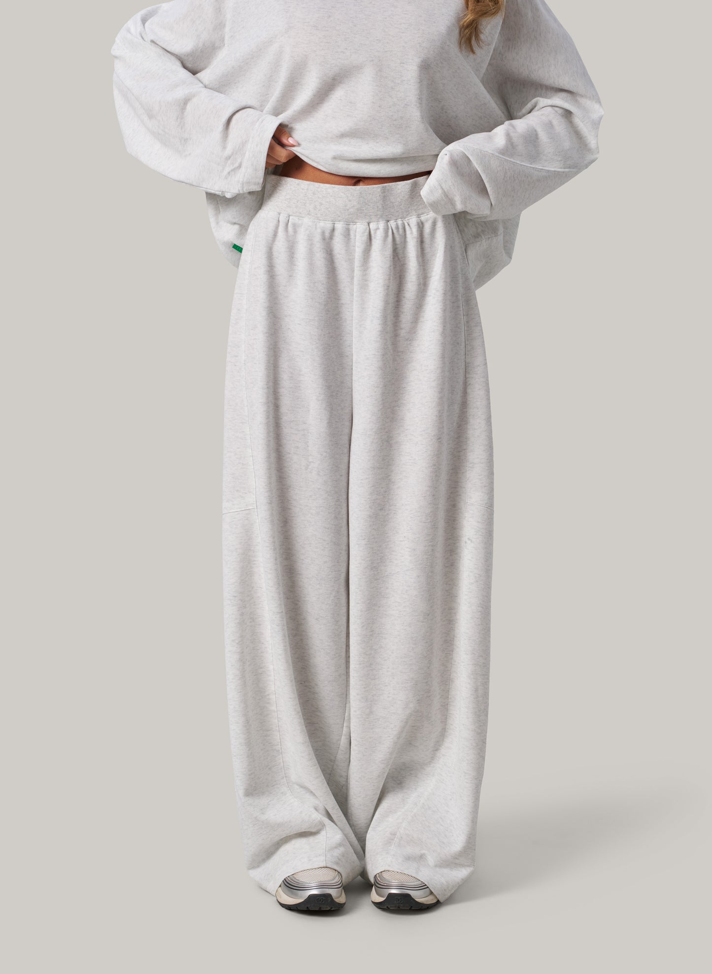 Person wearing a light grey sweatshirt and wide-leg pants on a plain background