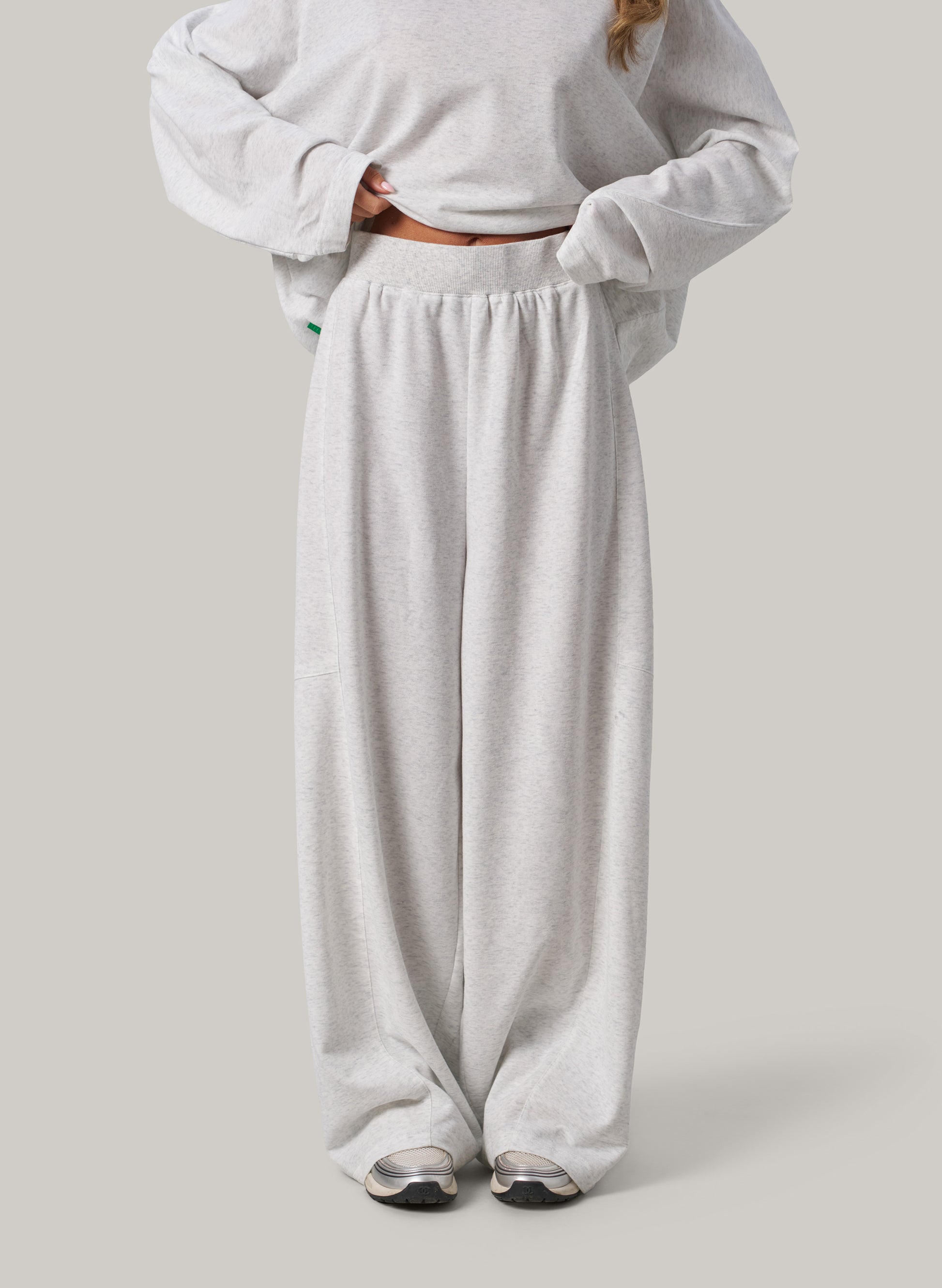 Person wearing a light grey sweatshirt and wide-leg pants on a plain background