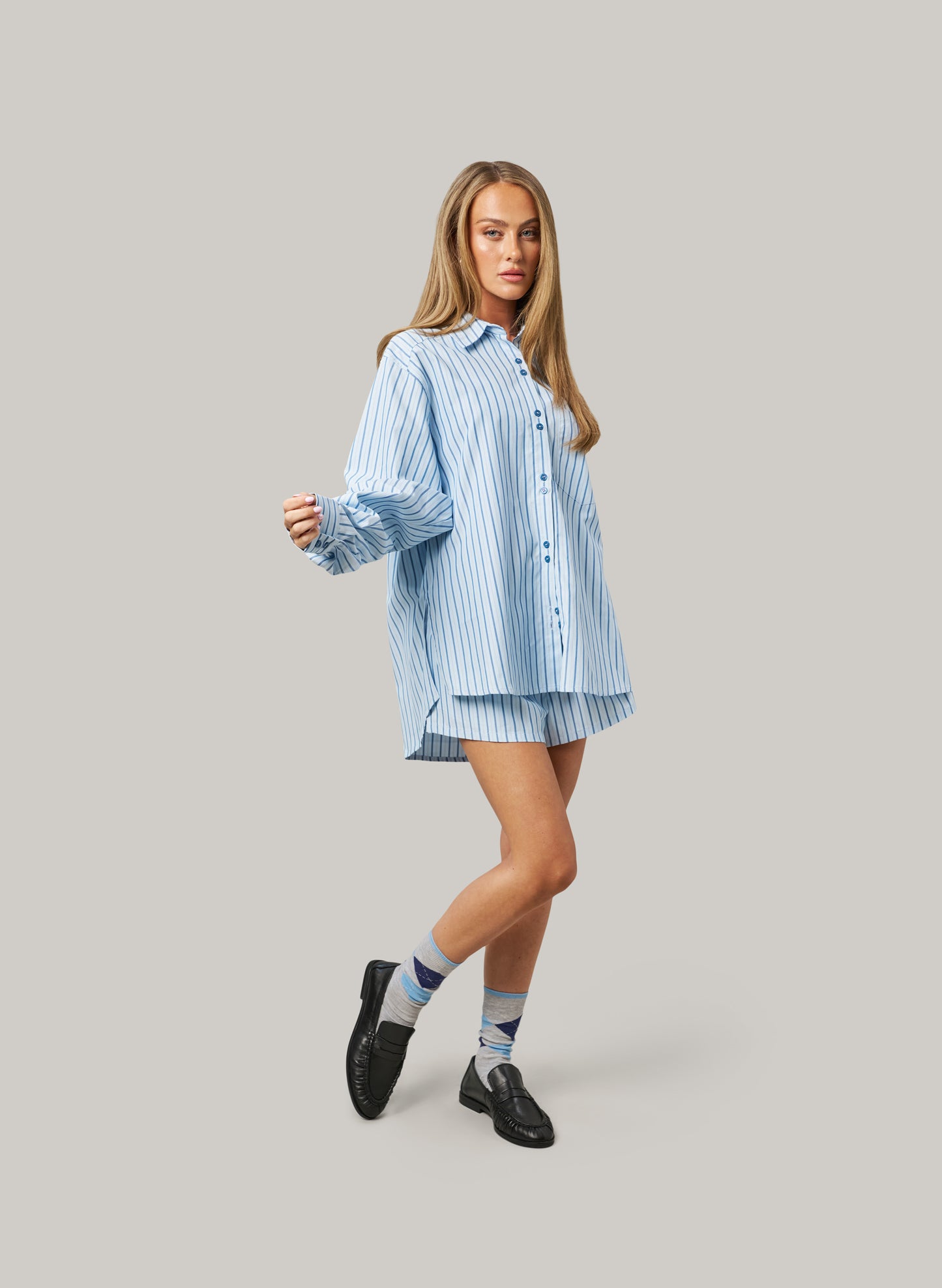 Woman wearing a blue striped shirt and shorts on a gray background