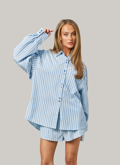 Woman wearing a light blue striped shirt and shorts set against a gray background