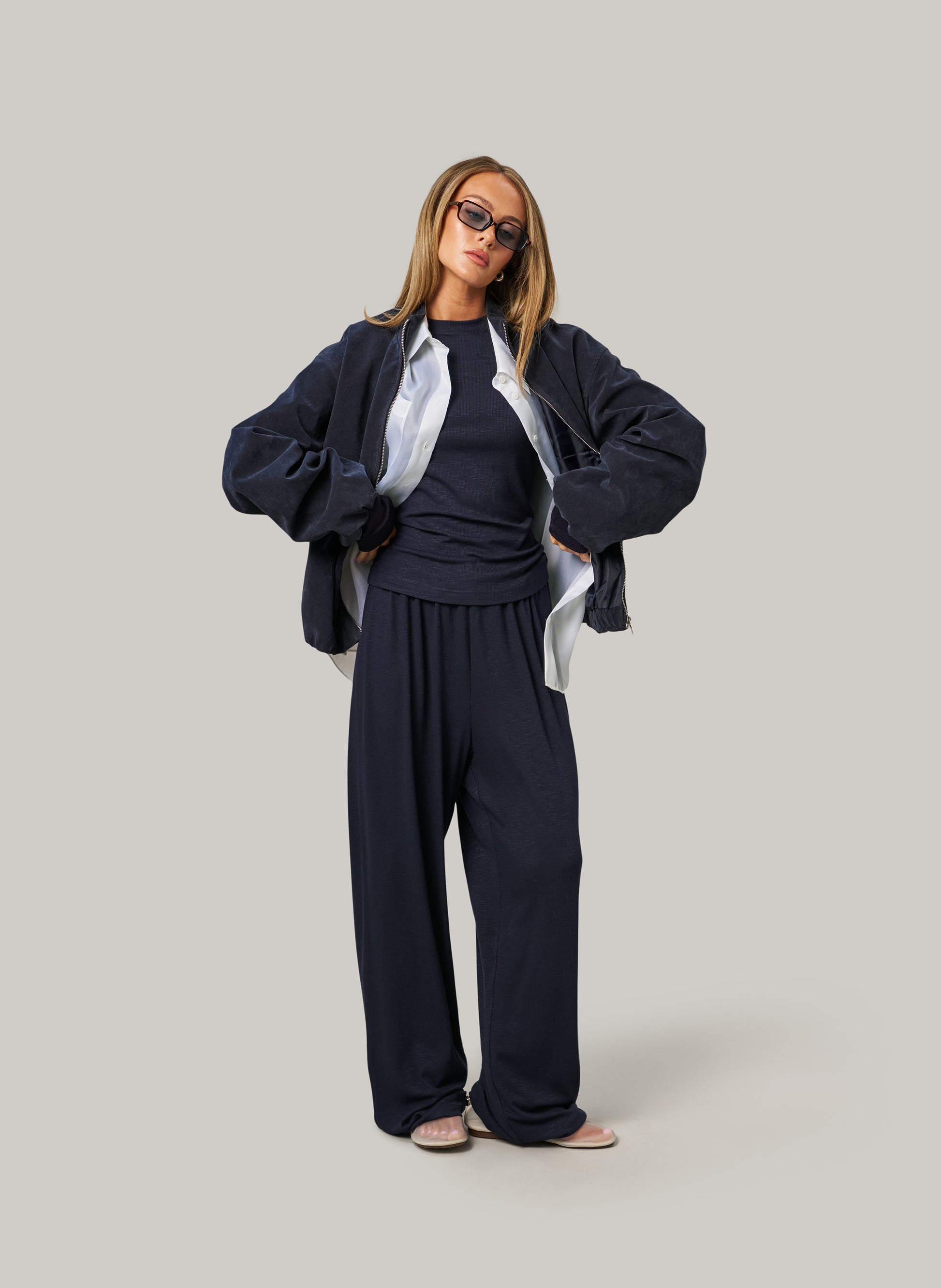 Person wearing a dark outfit with sunglasses on a plain background