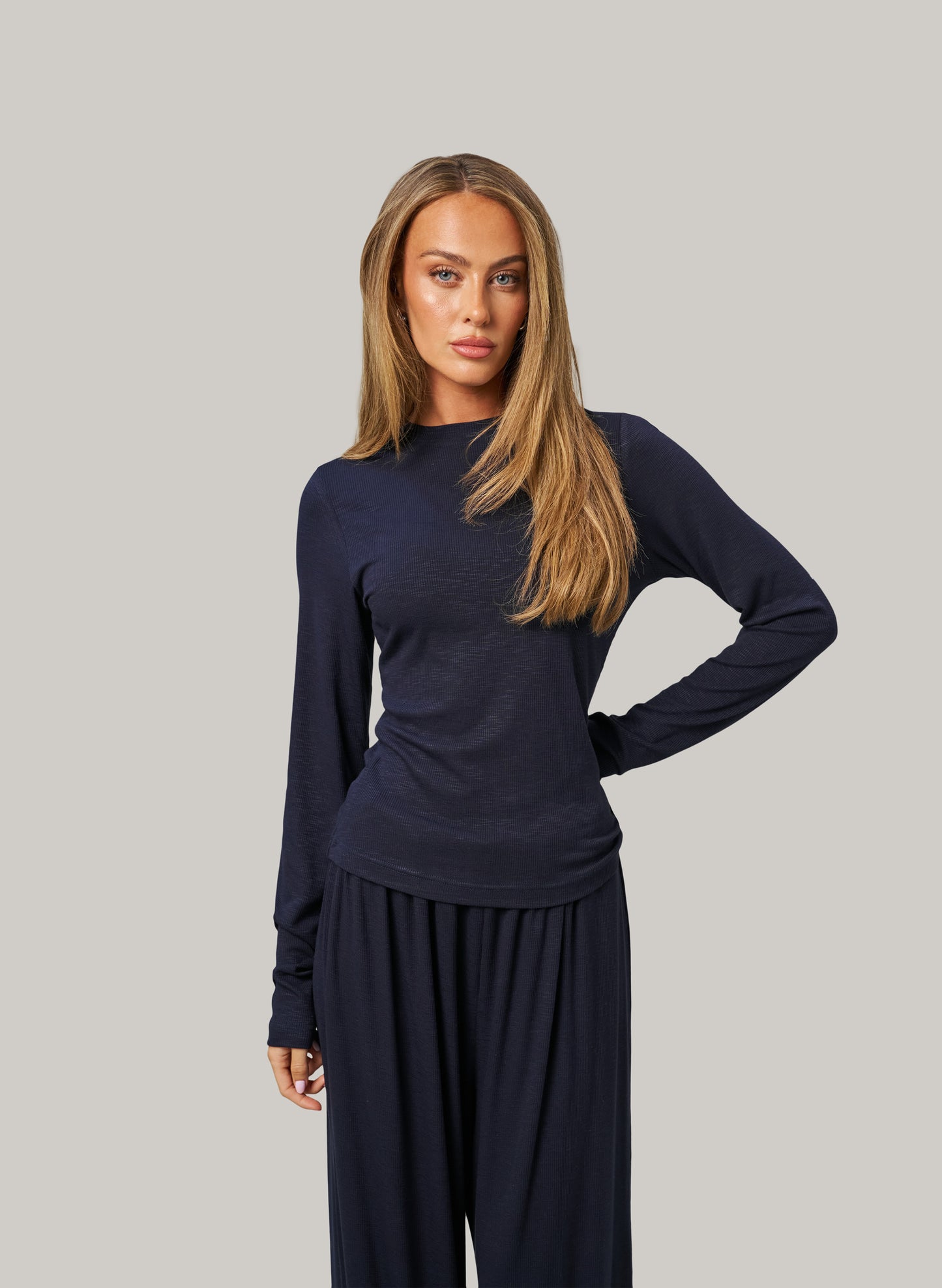 Woman wearing a navy long-sleeve top and pants on a gray background