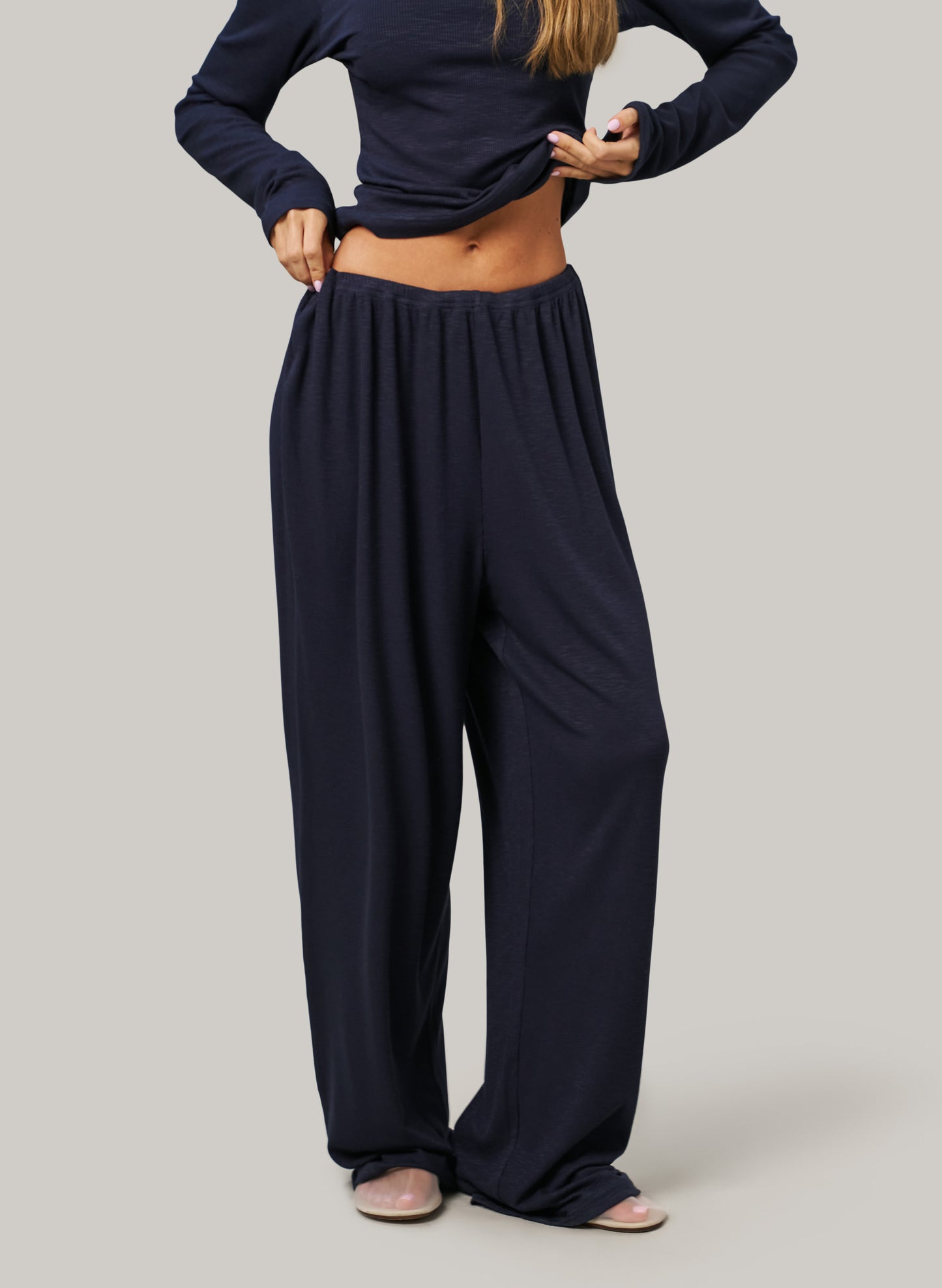 Person wearing navy blue high-waisted pants and long-sleeve top on a plain background