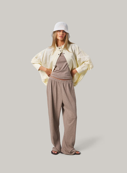 Woman wearing a light-colored jacket, brown top, and pants on a plain background