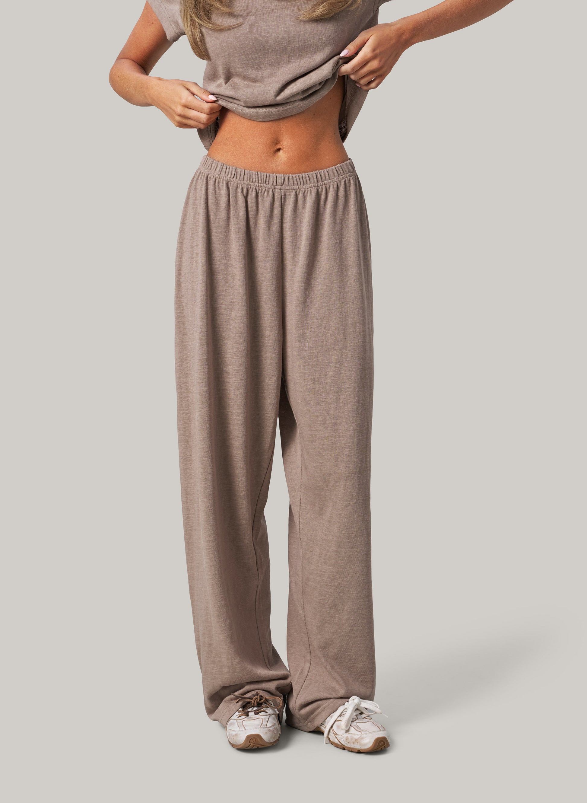 Person wearing beige lounge pants and a matching top on a plain background