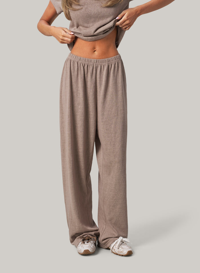 Person wearing beige lounge pants and a matching top on a plain background
