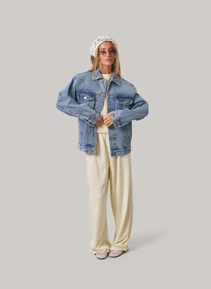 Person wearing a denim jacket, white top, and butter colour pants on a plain background