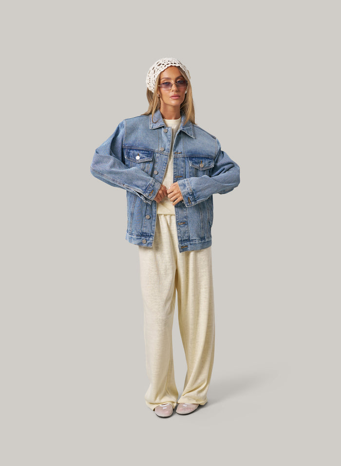 Person wearing a denim jacket, white top, and butter colour pants on a plain background