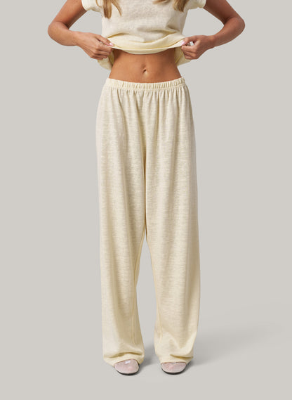 Person wearing butter colour pants and a white top on a grey background