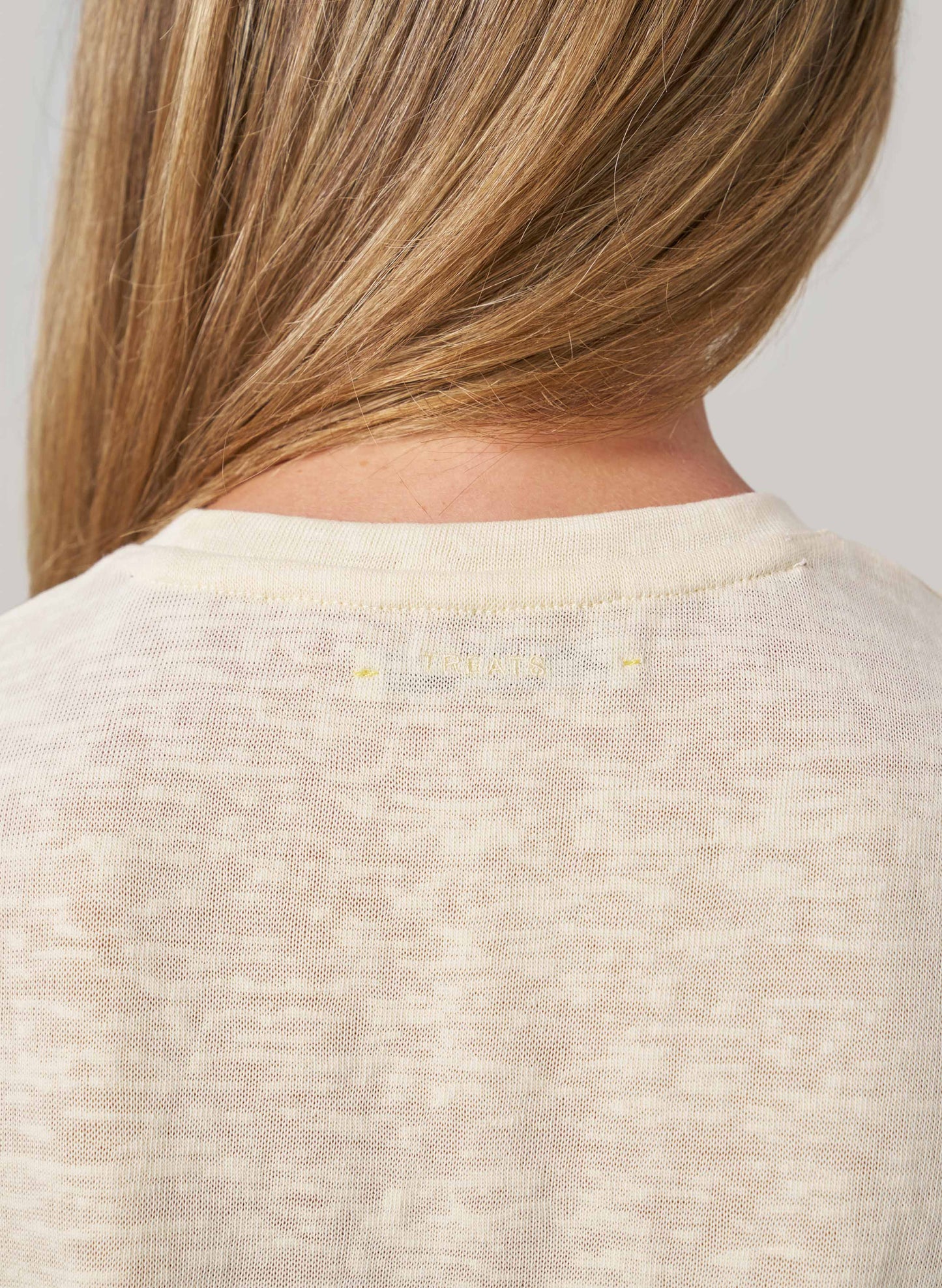 Close-up of a person wearing a butter colour sweater with a plain background