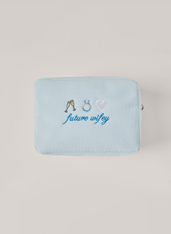 Light blue waffle-textured pouch with zipper closure, featuring embroidered champagne glasses, a ring, and a heart with the words ‘future wifey’ on the front