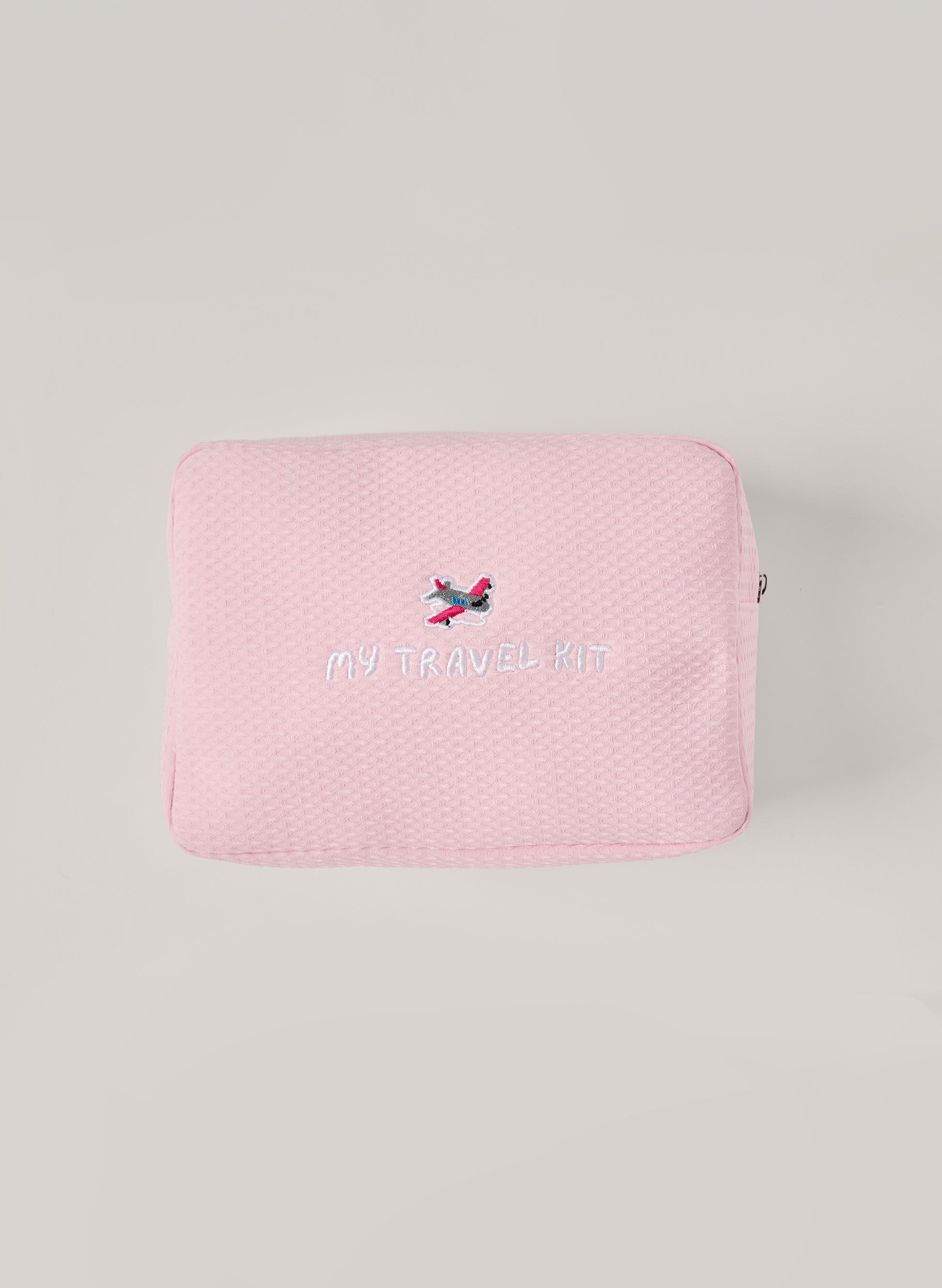 Light pink waffle-textured pouch with zipper closure, featuring an embroidered airplane and ‘my travel kit’ text on the front