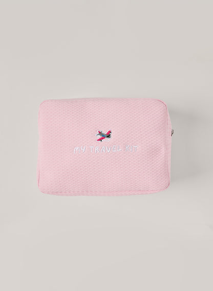 Light pink waffle-textured pouch with zipper closure, featuring an embroidered airplane and ‘my travel kit’ text on the front