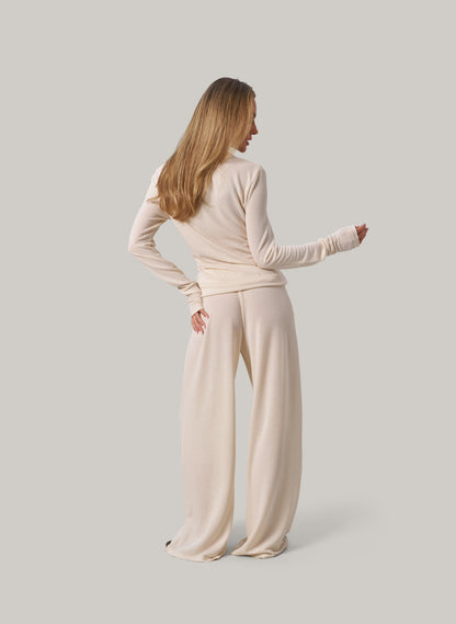 Woman wearing a cream outfit standing against a plain background