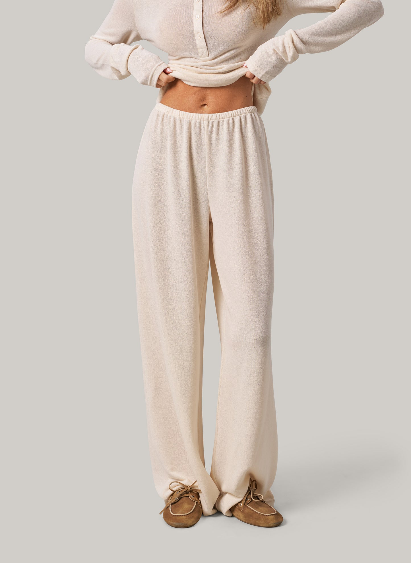 Person wearing cream pants and a matching top on a plain background