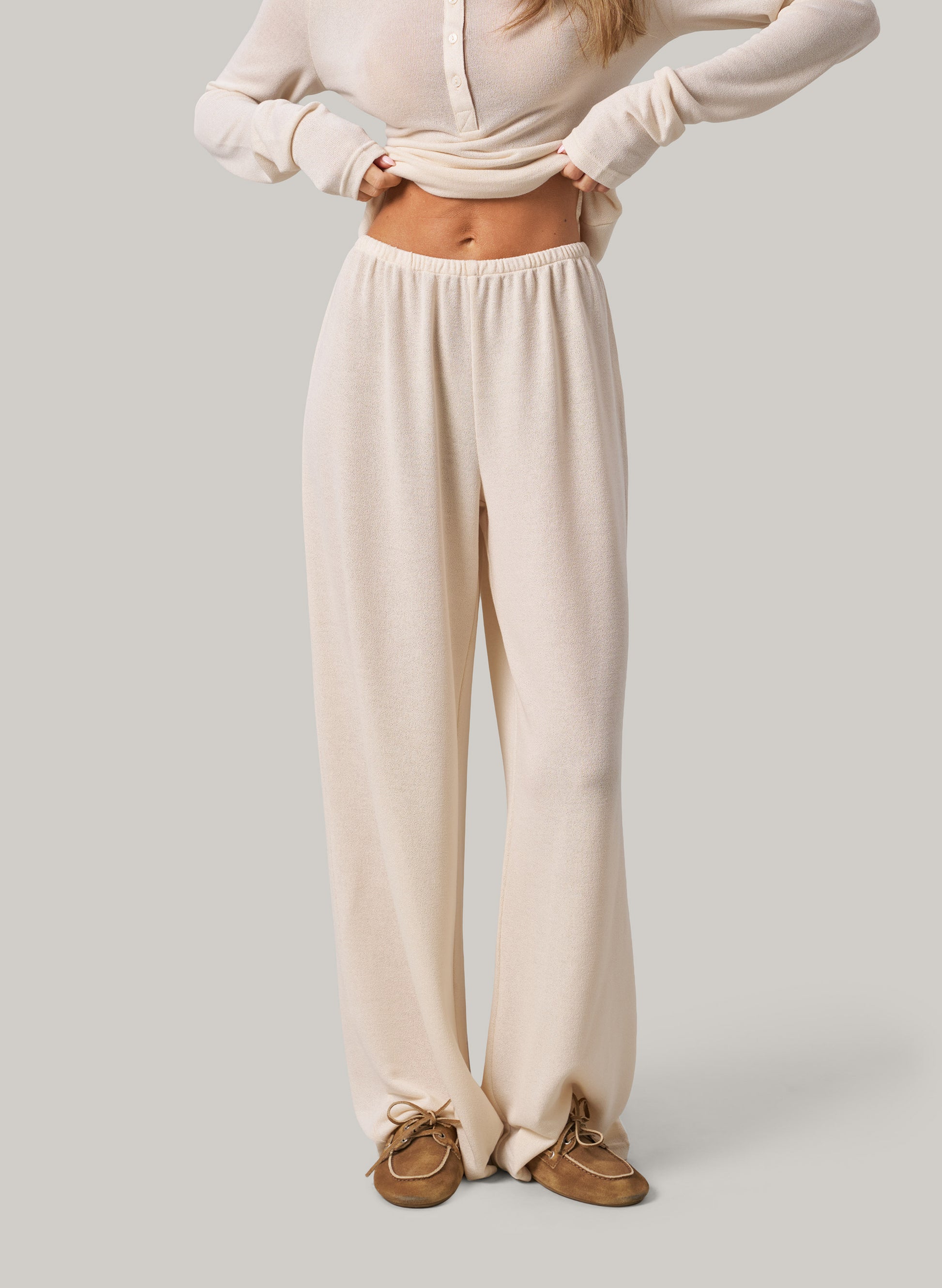 Person wearing cream pants and a matching top on a plain background