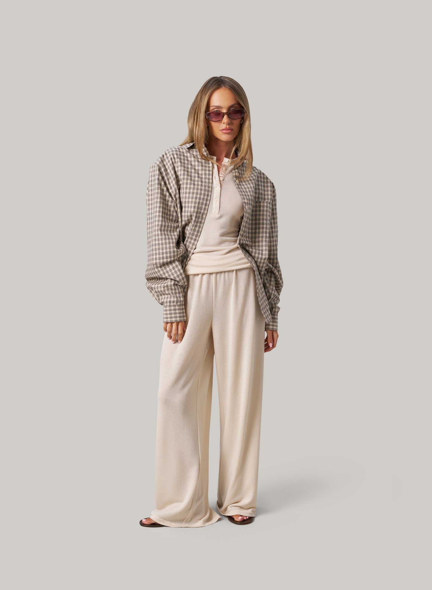 Woman wearing a plaid shirt and cream pants on a plain background