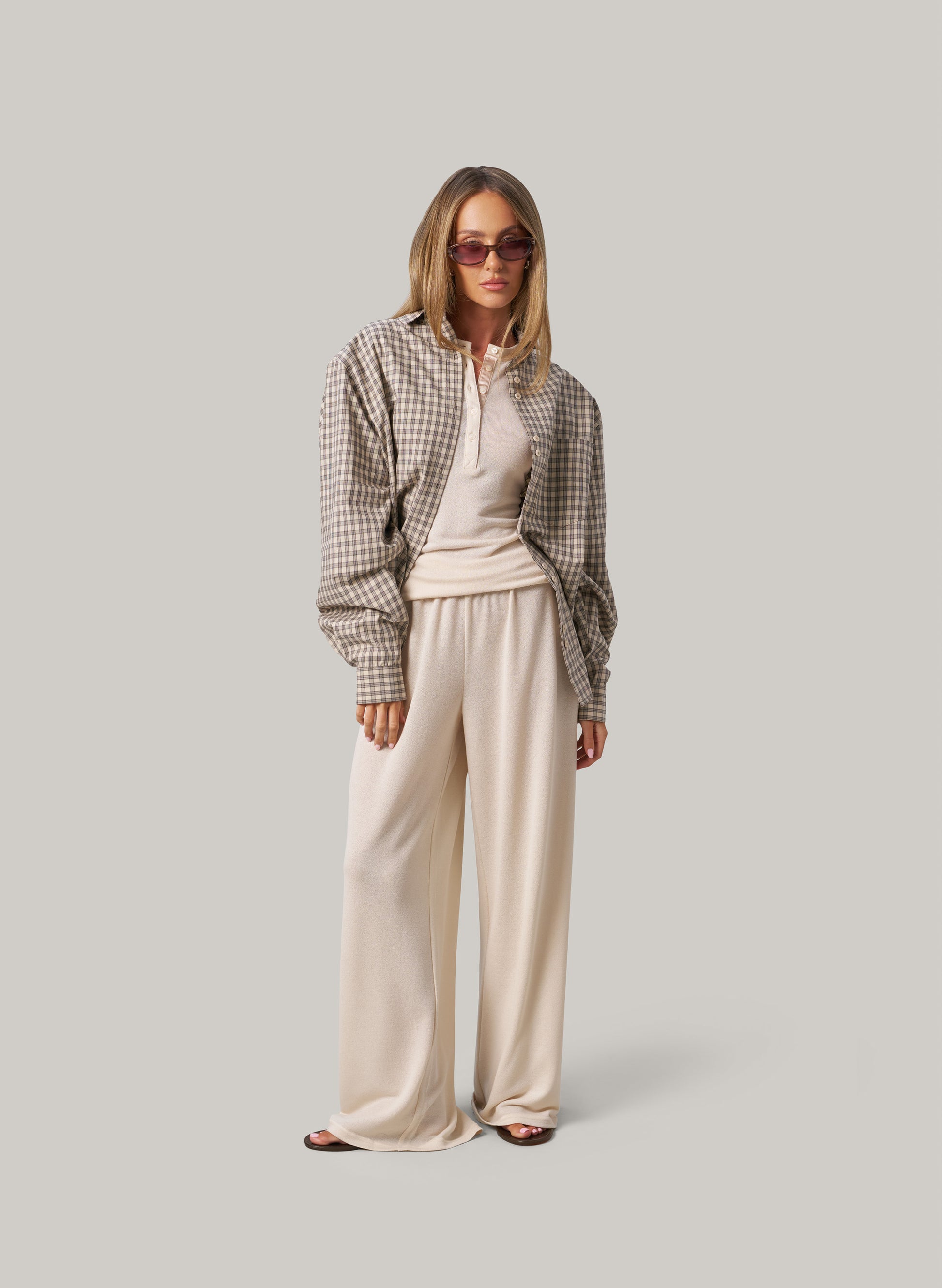 Woman wearing a plaid shirt and cream pants on a plain background