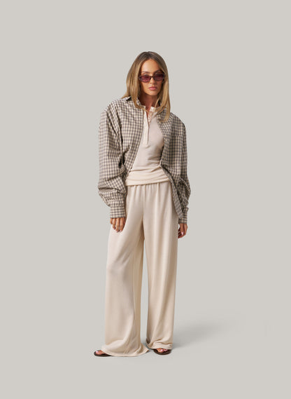 Woman wearing a plaid shirt and cream pants on a plain background