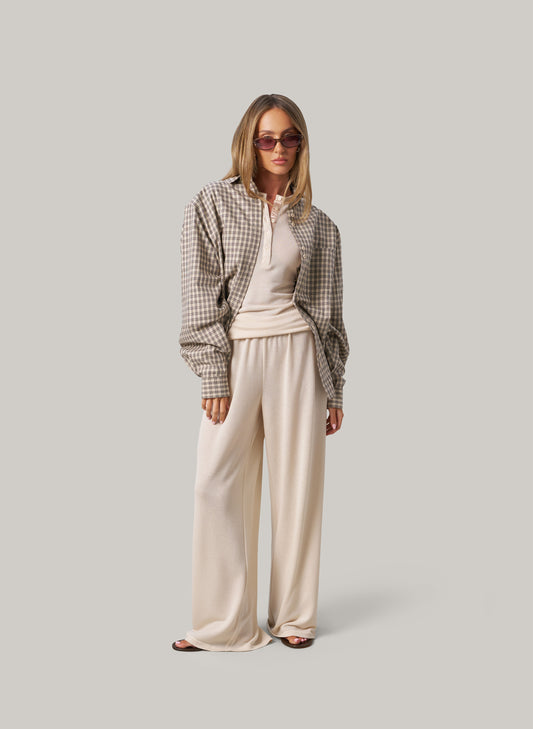 Woman wearing a plaid shirt and cream pants on a plain background