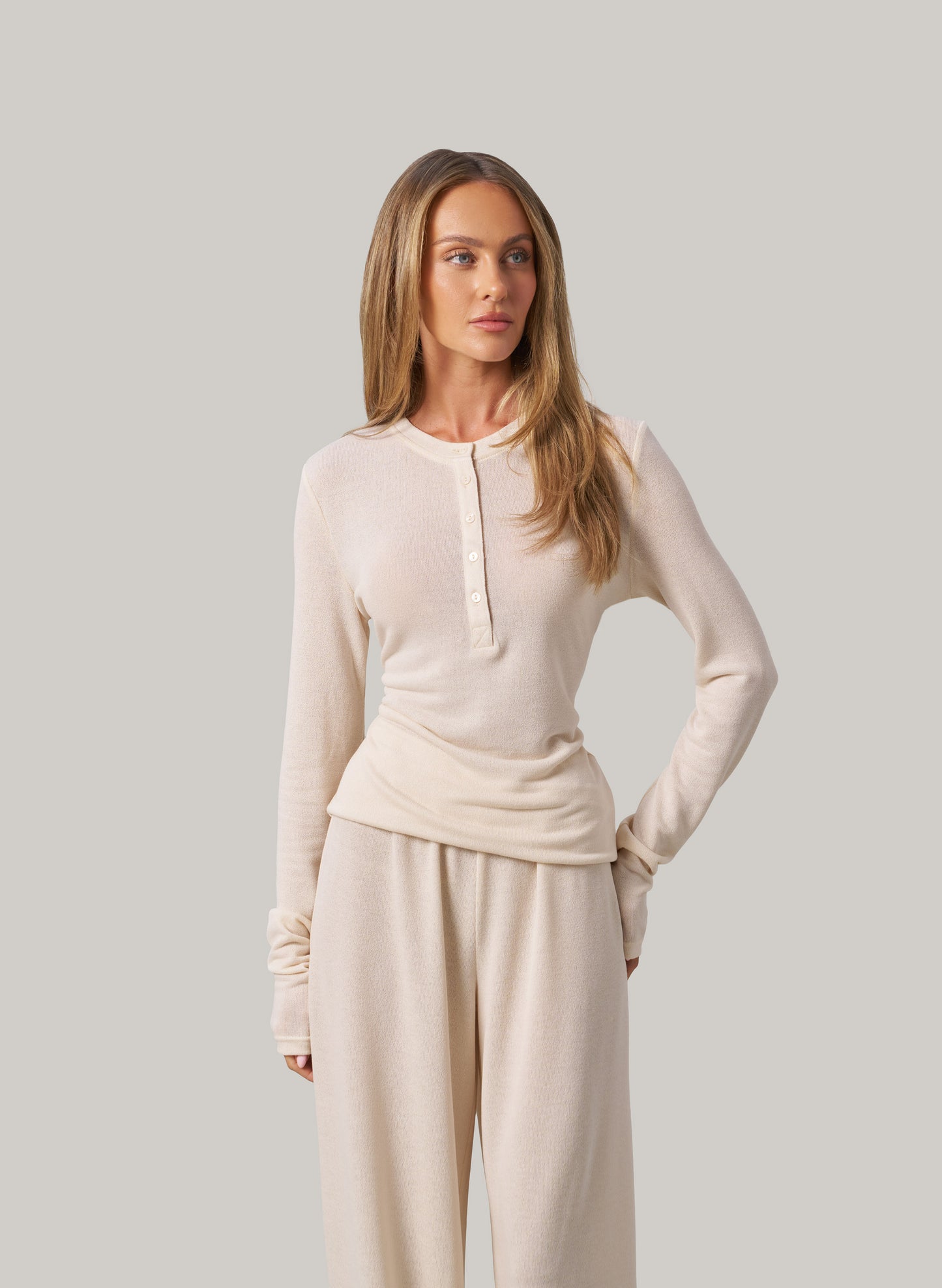 Woman wearing a cream long-sleeve top and pants against a plain background