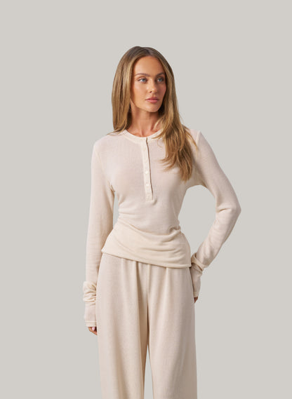 Woman wearing a cream long-sleeve top and pants against a plain background