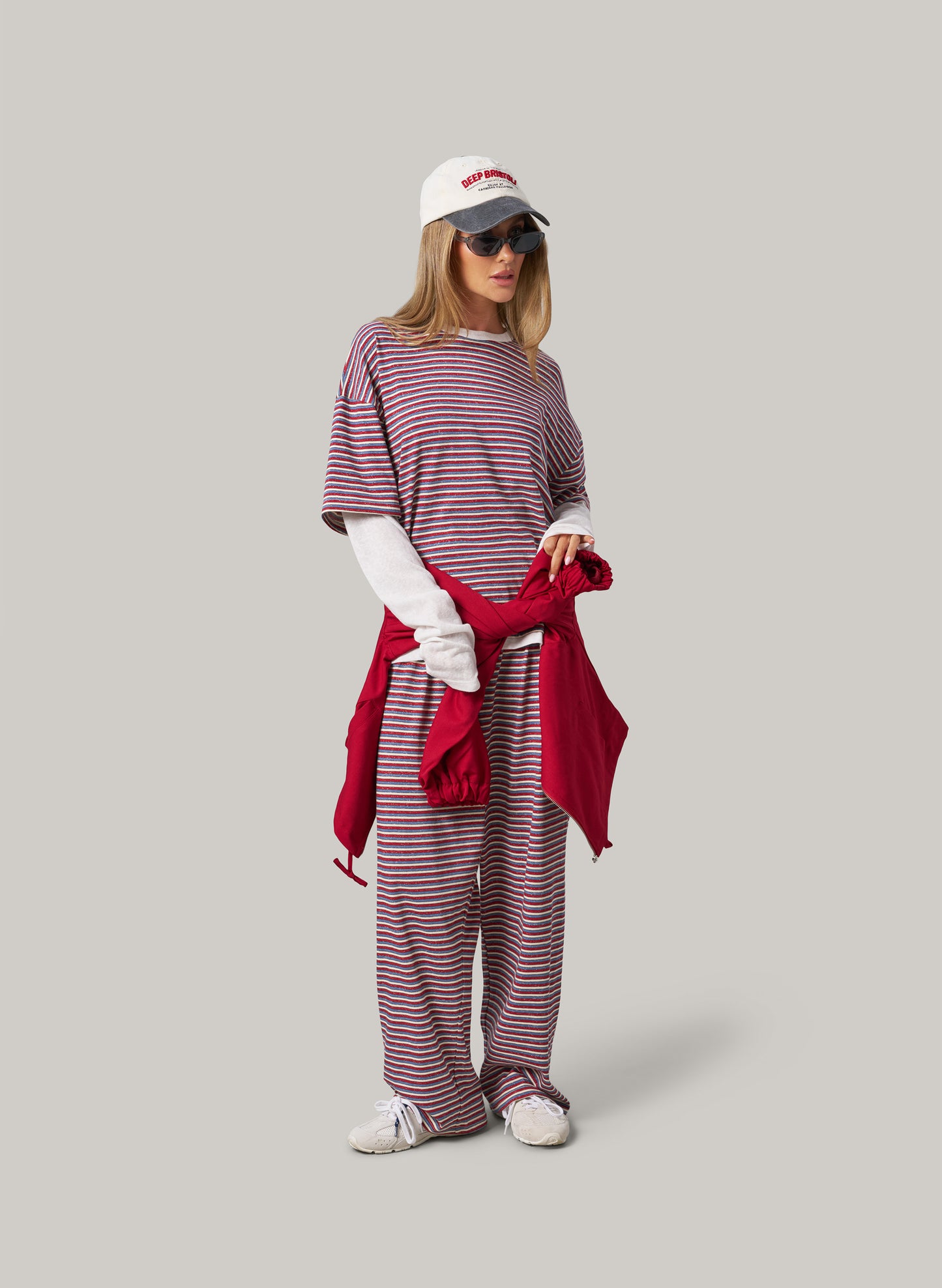 Woman wearing a striped outfit with a red scarf and white cap on a grey background