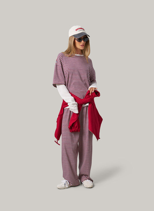 Woman wearing a striped outfit with a red scarf and white cap on a grey background