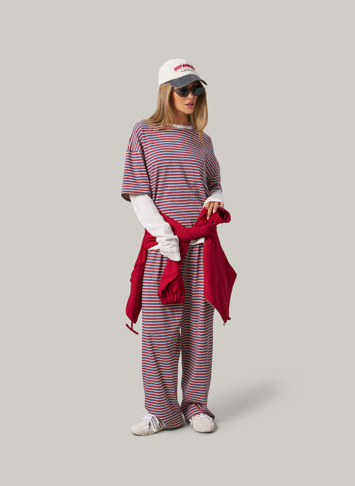 Woman wearing a striped outfit with a red scarf and white cap on a grey background