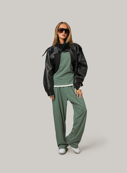 Woman wearing a black jacket, green striped sweater, and matching pants on a light gray background