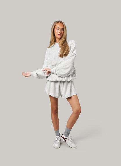 Woman wearing a grey sweatshirt and shorts set on a plain background