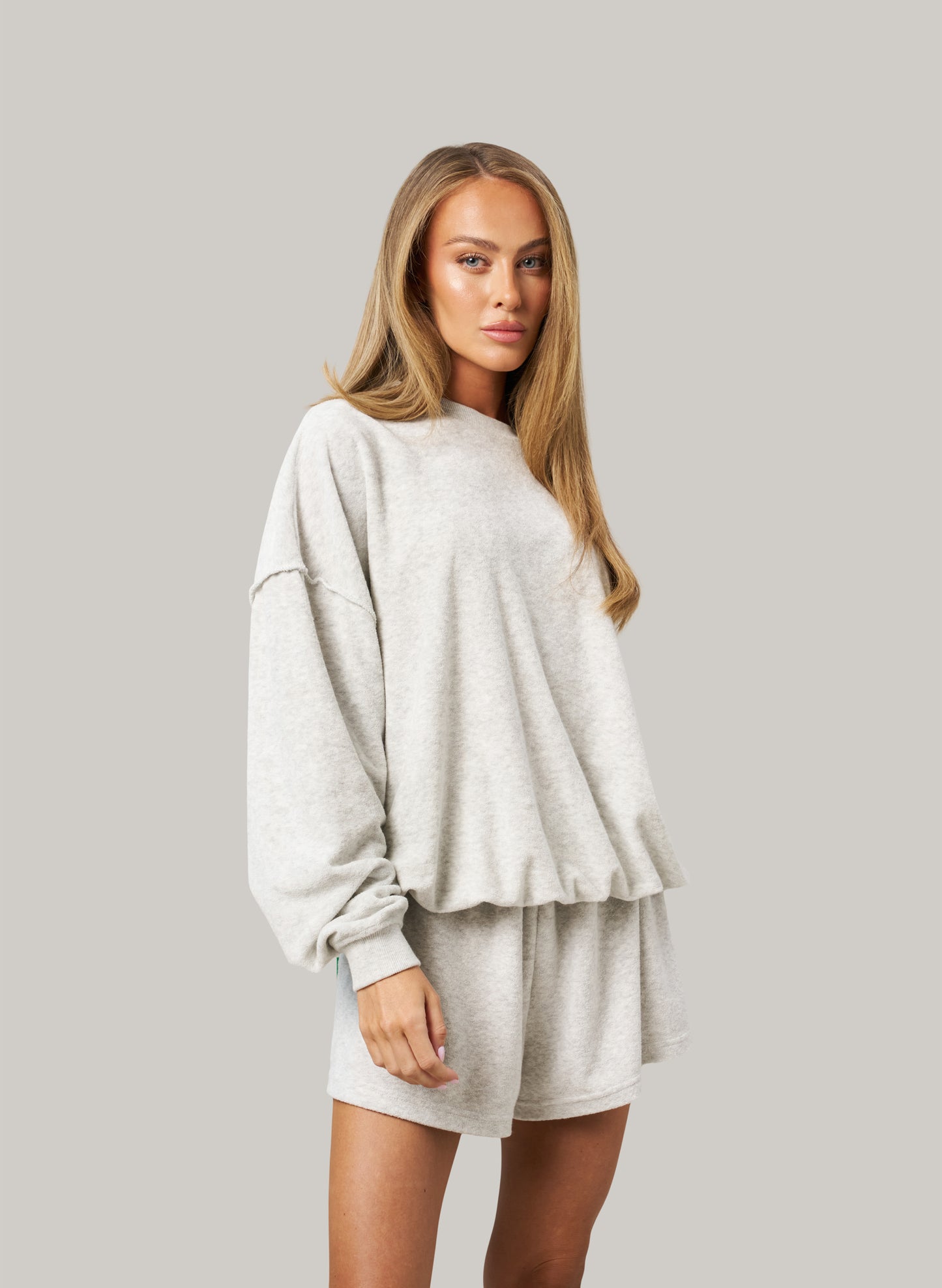 Woman wearing a light grey oversized sweatshirt and shorts set on a plain background