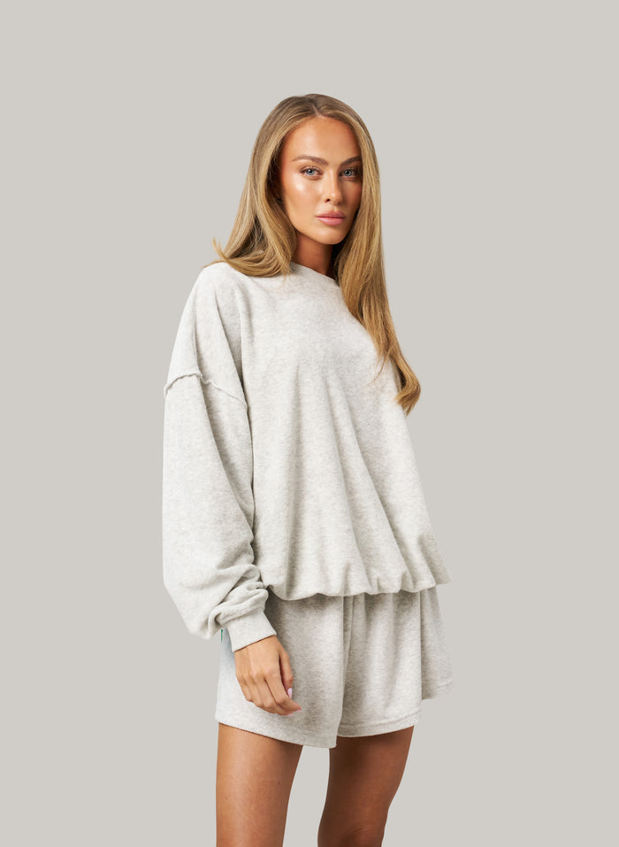 Woman wearing a light grey oversized sweatshirt and shorts set on a plain background