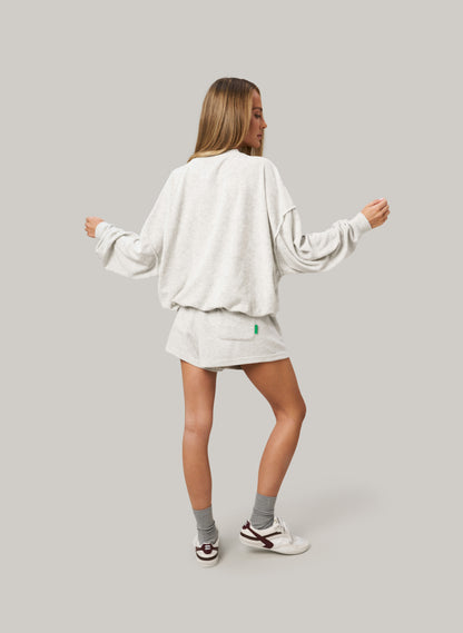 Woman wearing a grey sweatshirt and skirt set on a plain background