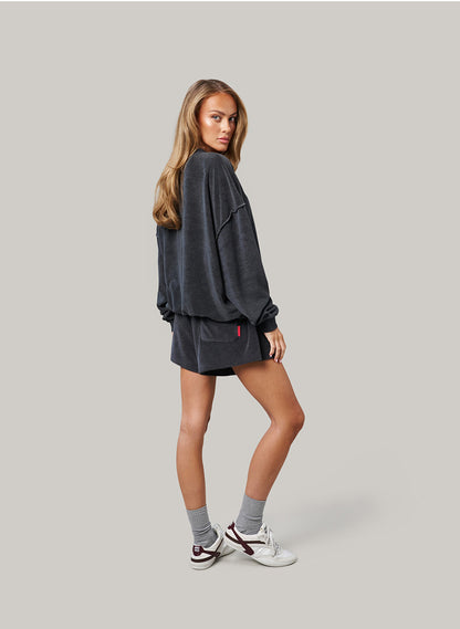 Woman wearing a dark navy oversized sweatshirt and shorts set on a light grey background